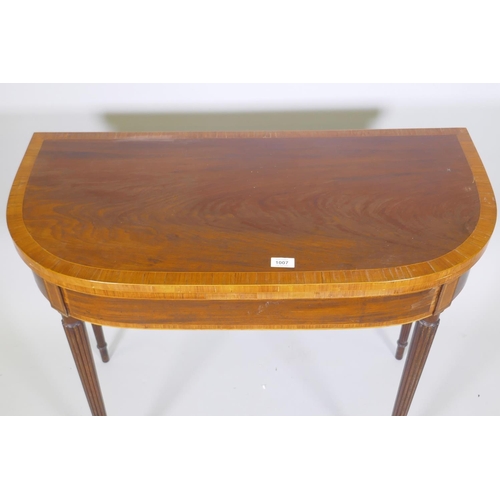 1007 - A Georgian mahogany D shaped card table, with cross banded top and frieze, raised on reeded tapering... 