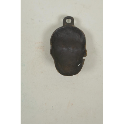 254 - A Tibetan bronze citipati death mask pendant, and a pendant in the form of a wrathful deity