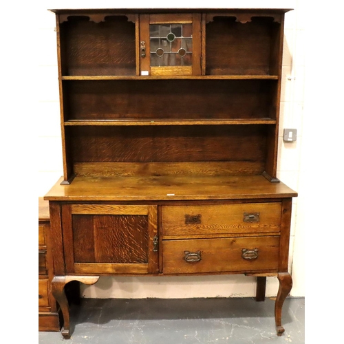 557 - An Arts and Crafts oak dresser, the sideboard base asymmetric with drawers and cupboard, plate rack ... 