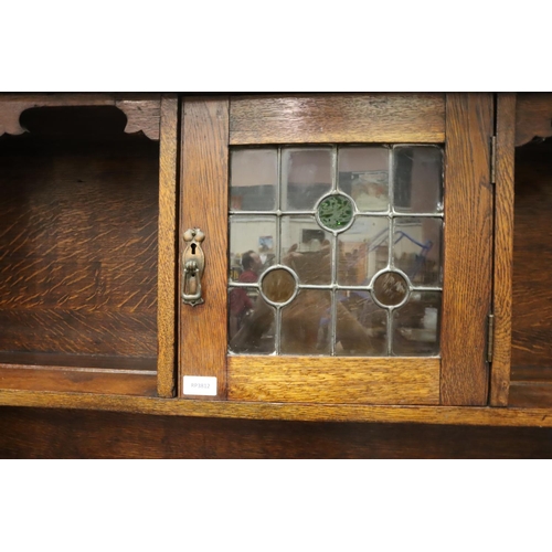 557 - An Arts and Crafts oak dresser, the sideboard base asymmetric with drawers and cupboard, plate rack ... 