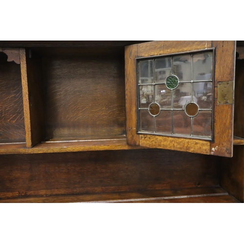 557 - An Arts and Crafts oak dresser, the sideboard base asymmetric with drawers and cupboard, plate rack ... 