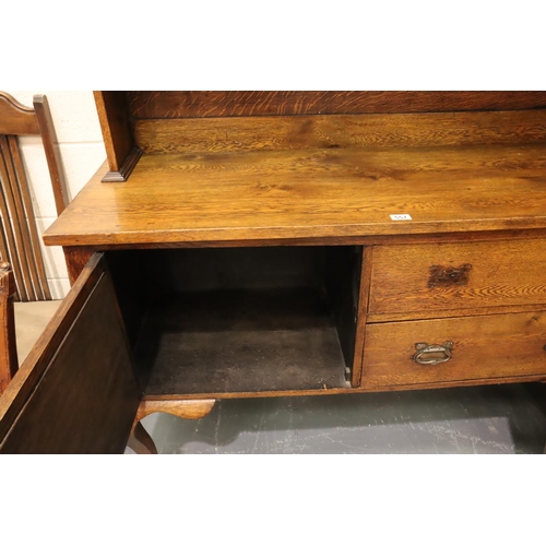 557 - An Arts and Crafts oak dresser, the sideboard base asymmetric with drawers and cupboard, plate rack ... 