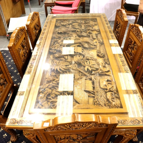 500 - A deeply carved substantial Oriental hardwood dining table with plate glass top displaying figures a... 