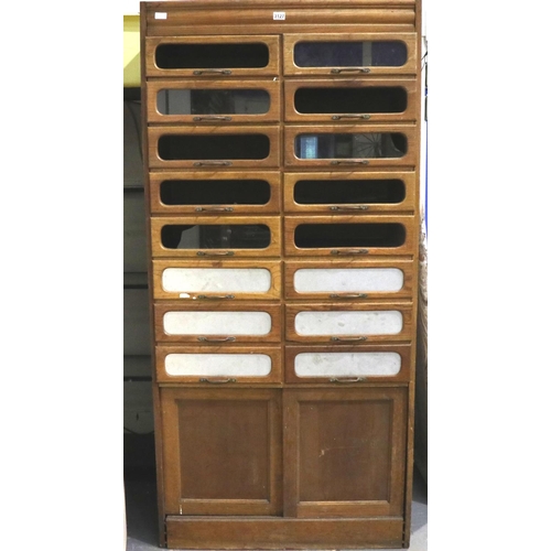 3127 - An early 20th century oak shopfitting haberdashery cabinet, having sixteen drawers above a cupboard ... 