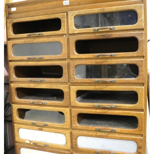 3127 - An early 20th century oak shopfitting haberdashery cabinet, having sixteen drawers above a cupboard ... 