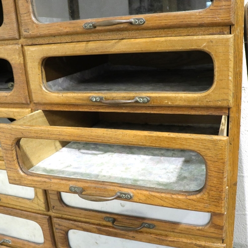 3127 - An early 20th century oak shopfitting haberdashery cabinet, having sixteen drawers above a cupboard ... 