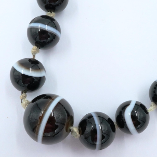 3070 - A single strand of graduated and polished brown manao agate beads formed as a necklace with knotted ... 