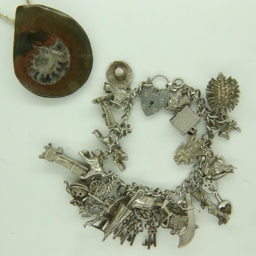 11 - Silver charm bracelet mounted with twenty-five charms, 66g, and a fossil pendant on a silver neck ch... 