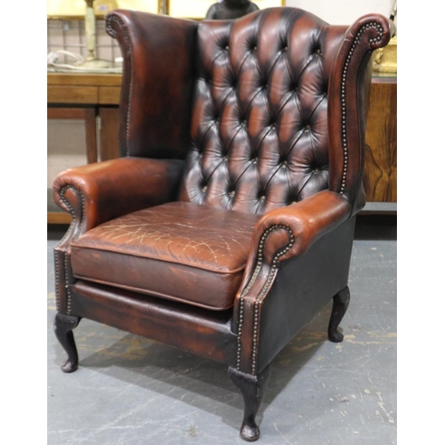 2089 - A 20th century wing-back chesterfield fire side chair in ox blood red, structurally sound but requir... 