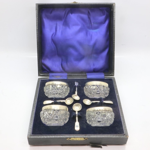 110 - A set of four cut glass open salts, each with a silver rim and associated condiment spoon, within a ... 