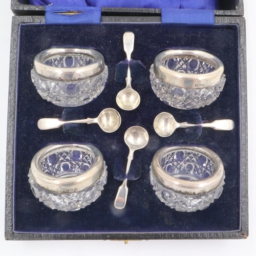 79 - A set of four cut glass open salts, each with a silver rim and associated condiment spoon, within a ... 