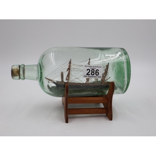 286 - Ship in a glass bottle on a wooden display stand, length 24cm. UK P&P Group 2 (£20+VAT for the first... 