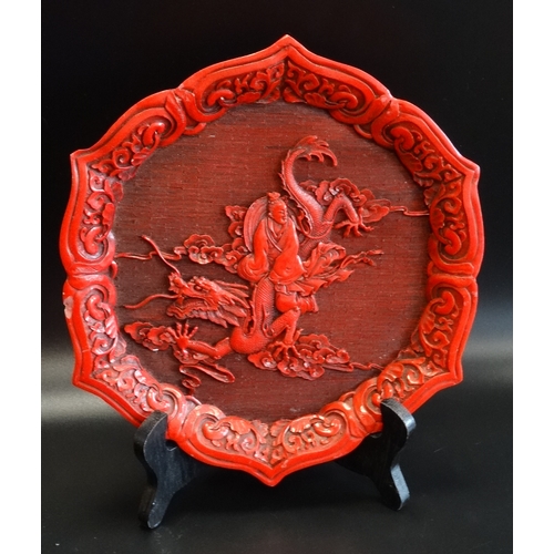 268 - CINNABAR WALL PLAQUE
with a shaped border decorated with scrolls around a central dragon with a man ... 