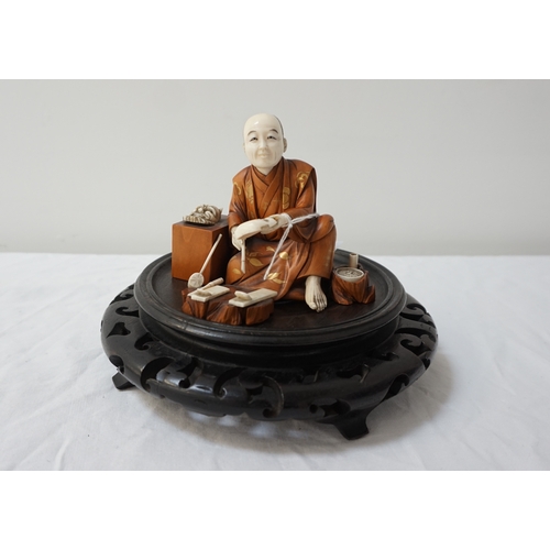 283 - CARVED JAPANESE IVORY AND BOXWOOD OKIMINO
of a Noh mask maker, seated with his masks and tools aroun... 