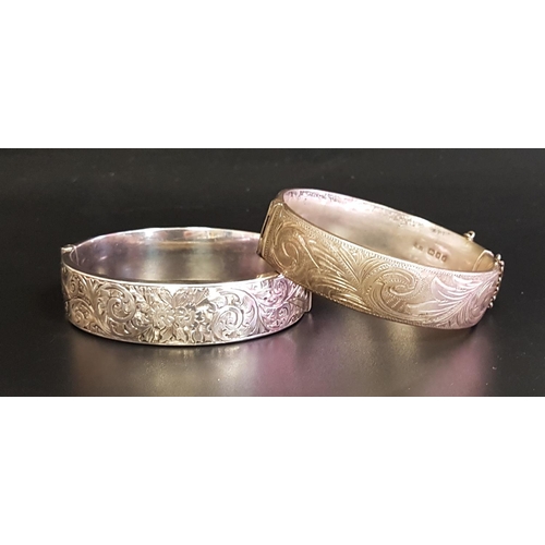 126 - TWO SILVER HINGED BANGLES
both with engraved scroll decoration, one with safety chain, London 1959 a... 