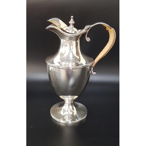 190 - GEORGE V SILVER CLARET JUG
with a hinged lid and rattan covered handle, raised on a circular foot, 2... 