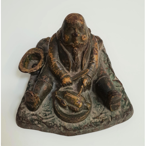 360 - VINTAGE CAST IRON INKWELL
depicting a large man seated with his hat beside him, eating a roast chick... 