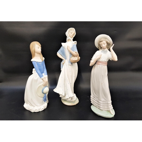 311 - THREE NAO FIGURINES
comprising a girl holding her hat, 28cm high, a girl holding a basket of flowers... 