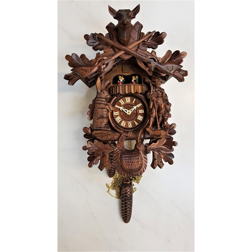 384 - GERMAN BLACK FOREST WALL CLOCK
in walnut and decorated with rifles, animals, hunter and oak leaves, ... 