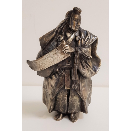 318 - JAPANESE SILVERED BRONZE OF A SHINTO PRIEST
wearing flowing robes and holding a scroll, with charact... 