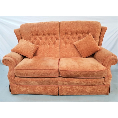 384 - TWO SEAT SOFA
with a shaped button back and scroll arms, covered in a dark peach floral chenille