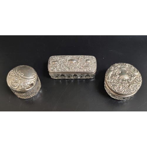 158 - THREE EARLY 20th CENTURN SILVER TOPPED GLASS DRESSING TABLE POTS
all with profuse scroll decoration ... 