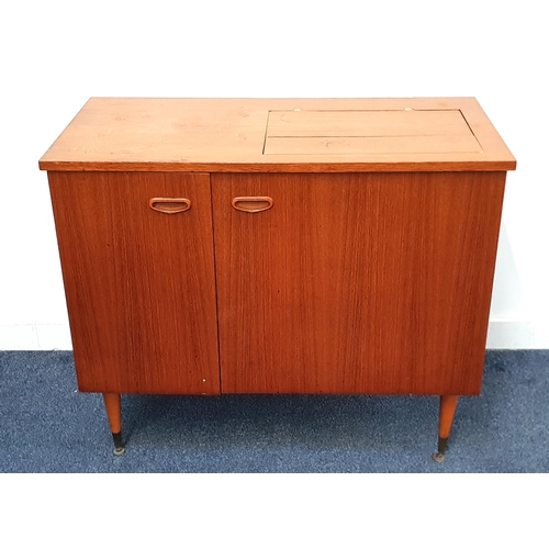 TEAK SEWING MACHINE CABINET
with a fold over flap top above a pair of cupboard doors, standing on turned tapering supports, 76.5cm x 90cm x 43cm