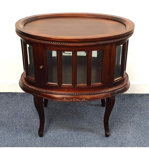 457 - TEAK VITRINE TABLE
with an oval moulded top above a glass panelled body with opposing doors, standin... 