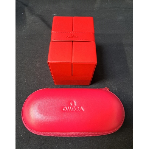 OMEGA RED LEATHERETTE WATCH BOX
with a branded fold over closure strap, double flap opening lid with a cream branded oval watch cushion interior and two outer card cases, together with an Omega red travel case with zip fastening and foam inserts (2)
