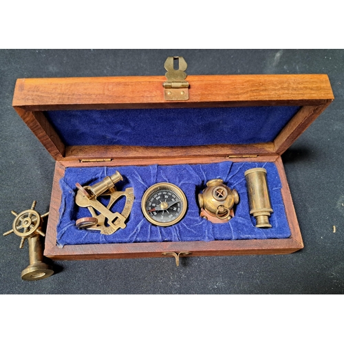 CASED SET OF MINIATURE BRASS NAUTICAL INSTUMENTS/ITEMS
comprising a sextant, a three draw telescope, a diver's helmet with copper detail and a compass, the wooden box with brass inlaid anchor detail; together with a miniature brass ship's wheel inset with compass to top of stand