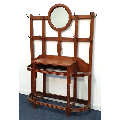 EDWARDIAN OAK HALL STAND
with a central circular bevelled mirror on a lattice work of panels with ten coat/hat hooks above a central shelf with drawer slot below, flanked by two shaped stick stands, 183cm x 122cm