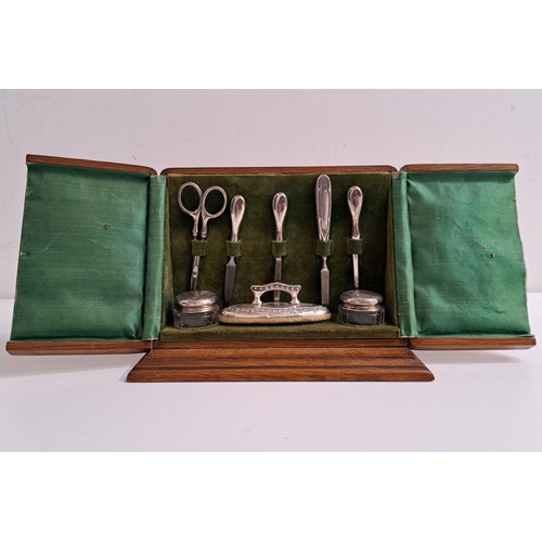 GEORGE V SILVER MANICURE SET
comprising a buffer, two files, tweezers, cuticle pusher and two silver topped jars, Chester 1922 and Birmingham 1910, in a fitted oak case with a satin and velvet interior
