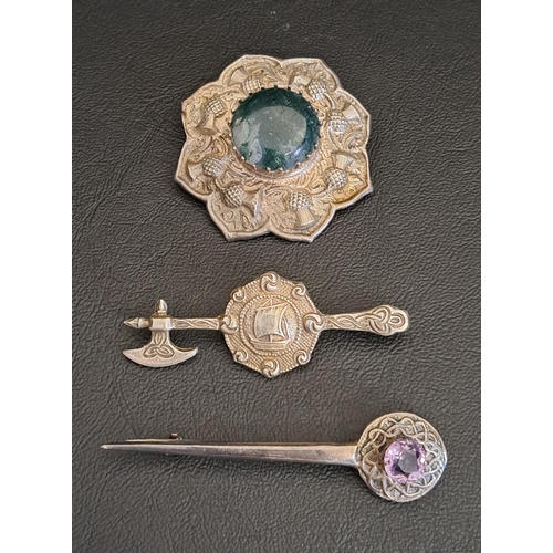 TWO CELTIC SILVER BROOCHES
one with central agate in relief thistle decorated surround, another in the form of an Axe and galleon decorated shield, with entwined Celtic decoration, and the other with amethyst set finial within an entwined border