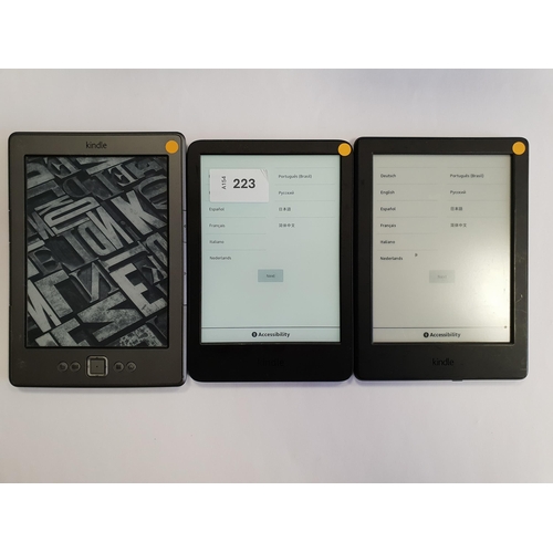 223 - THREE AMAZON KINDLE E-READERS
comprising a Basic 4, serial number G092 AP03 2316 03LR; a Basic 2, se... 