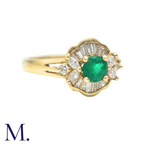 32 - An Emerald And Diamond Cluster Ring in 18k yellow gold, set with a principal round cut emerald accen... 