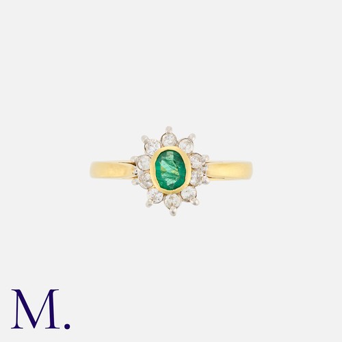 109 - An Emerald and Diamond Cluster Ring in 18K yellow gold, bezel set with an oval cut emerald to the ce... 