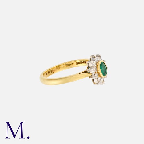 109 - An Emerald and Diamond Cluster Ring in 18K yellow gold, bezel set with an oval cut emerald to the ce... 