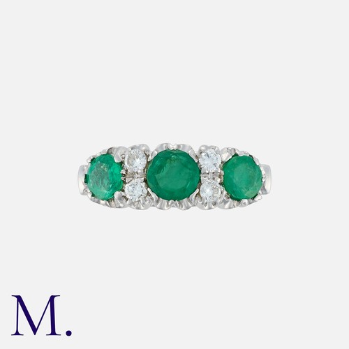 126 - An Emerald And Diamond Ring in 18k white gold, set with three round cut emeralds, accented by pairs ... 