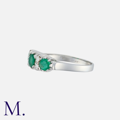 126 - An Emerald And Diamond Ring in 18k white gold, set with three round cut emeralds, accented by pairs ... 