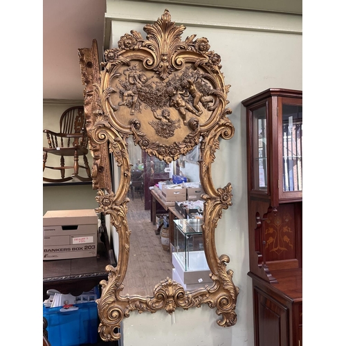 386 - Ornate gilt framed wall mirror with cherub decorated crest, 155cm by 69cm.