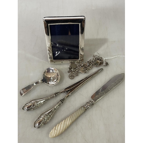 270 - Silver charm bracelet, silver and mother of pearl butter knife, small silver frame, glove stretchers... 