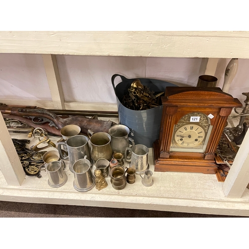 121 - Full shelf of brass and metalwares, mantel clock, model guns, martingales, pewter tankards, etc.