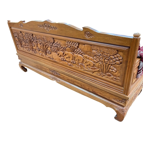 416 - Malaysian carved hardwood bench, the arms and back panel carved externally with tropical forest scen... 