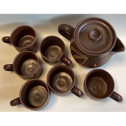 582 - A vintage stoneware tea set comprising a teapot and six cups in brown ground with wax resist patter.... 