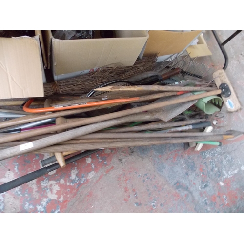 143 - A LARGE QUANTITY OF GARDENING HAND TOOLS - SPADES, FORKS, HOSE, RAKES ETC