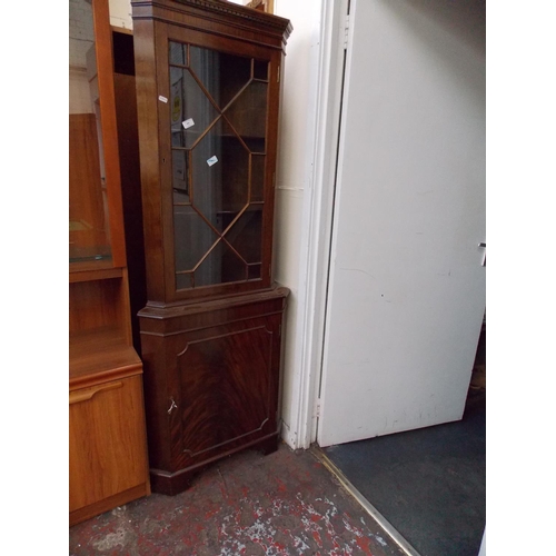 603 - A FLAMED MAHOGANY FREESTANDING CORNER CABINET WITH ONE GLAZED DOOR AND ONE LOWER DOOR