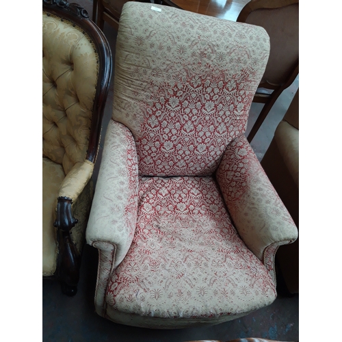 1229 - AN EARLY 20TH CENTURY LOW SEATED ARM CHAIR ON CASTER SUPPORTS WITH RED FLORAL UPHOLSTERY (IN NEED OF... 