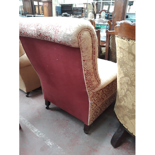 1229 - AN EARLY 20TH CENTURY LOW SEATED ARM CHAIR ON CASTER SUPPORTS WITH RED FLORAL UPHOLSTERY (IN NEED OF... 