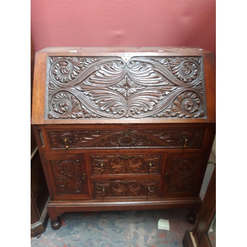 1117 - A JACOBEAN REVIVAL HEAVILY CARVED OAK BUREAU WITH TWO LOWER DOORS, TWO SHORT DRAWERS AND ONE LONG DR... 