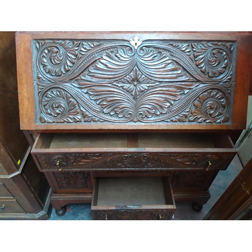 1117 - A JACOBEAN REVIVAL HEAVILY CARVED OAK BUREAU WITH TWO LOWER DOORS, TWO SHORT DRAWERS AND ONE LONG DR... 